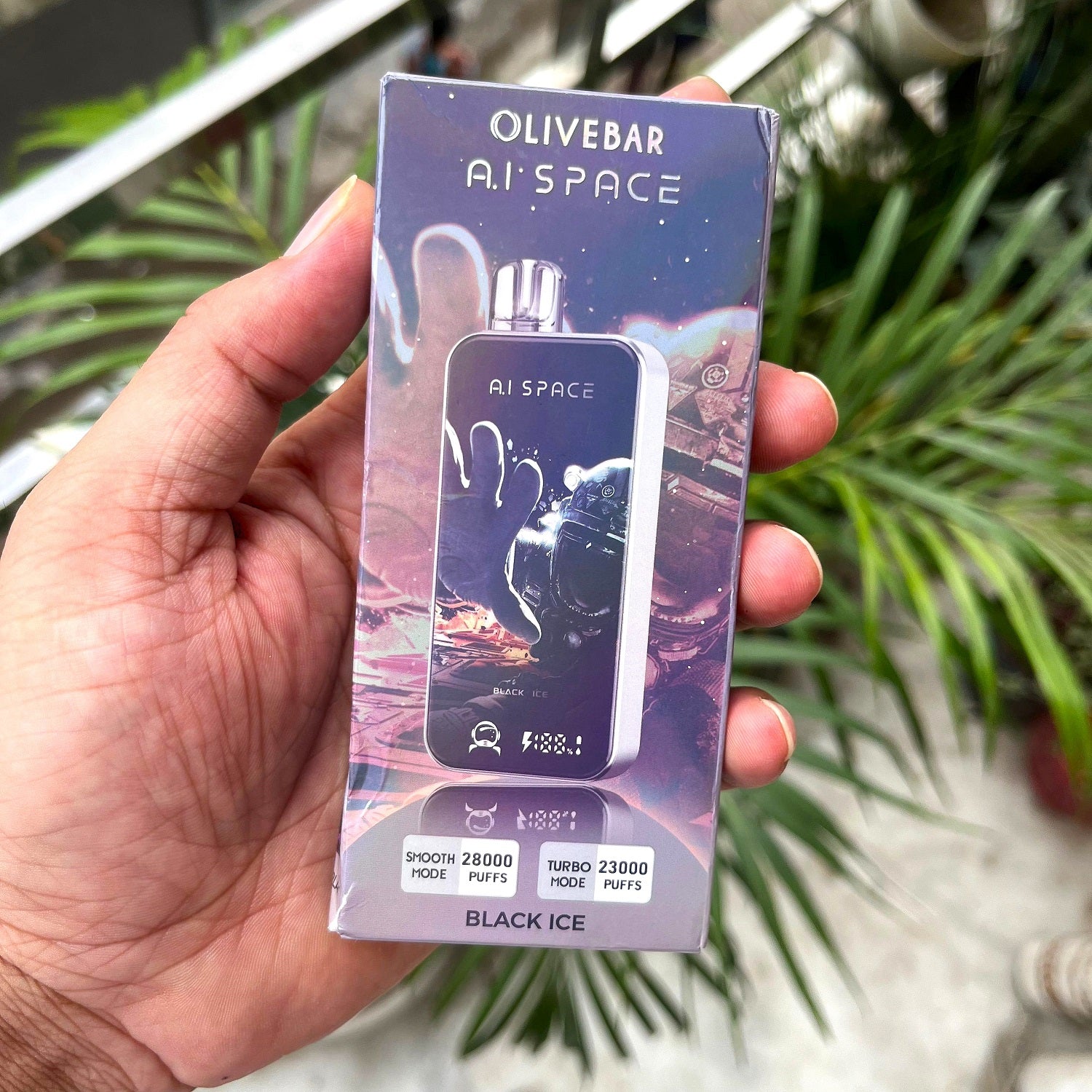 Olivebar A.I. Space vape device packaging held in a hand with a blurred green plant background
