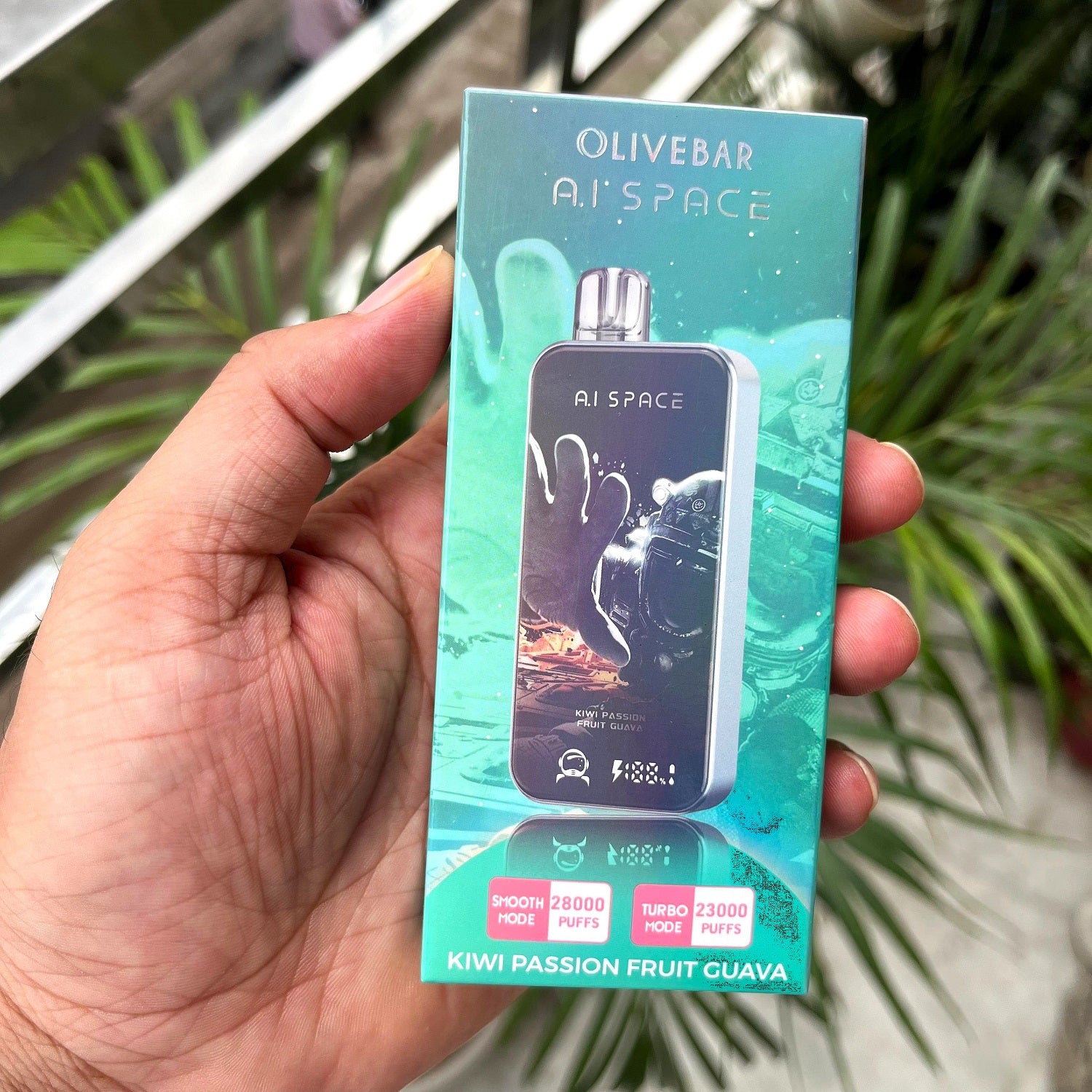 Hand holding a box of Olivebar AI'SPACE vape Kiwi passion fruit guava device with a green and blue design.