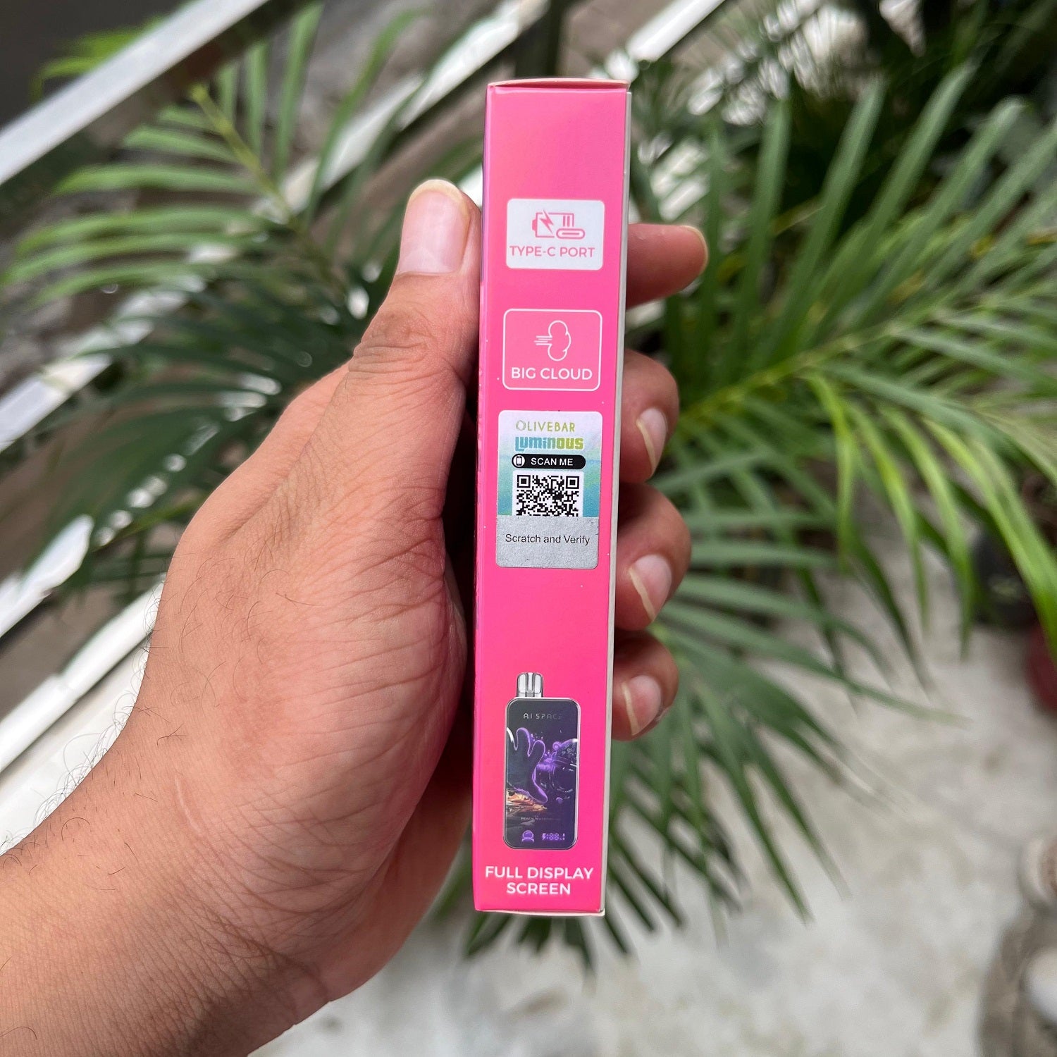 Hand holding a Olivebar AI Space device packaging with text and QR code, against a blurred outdoor background.