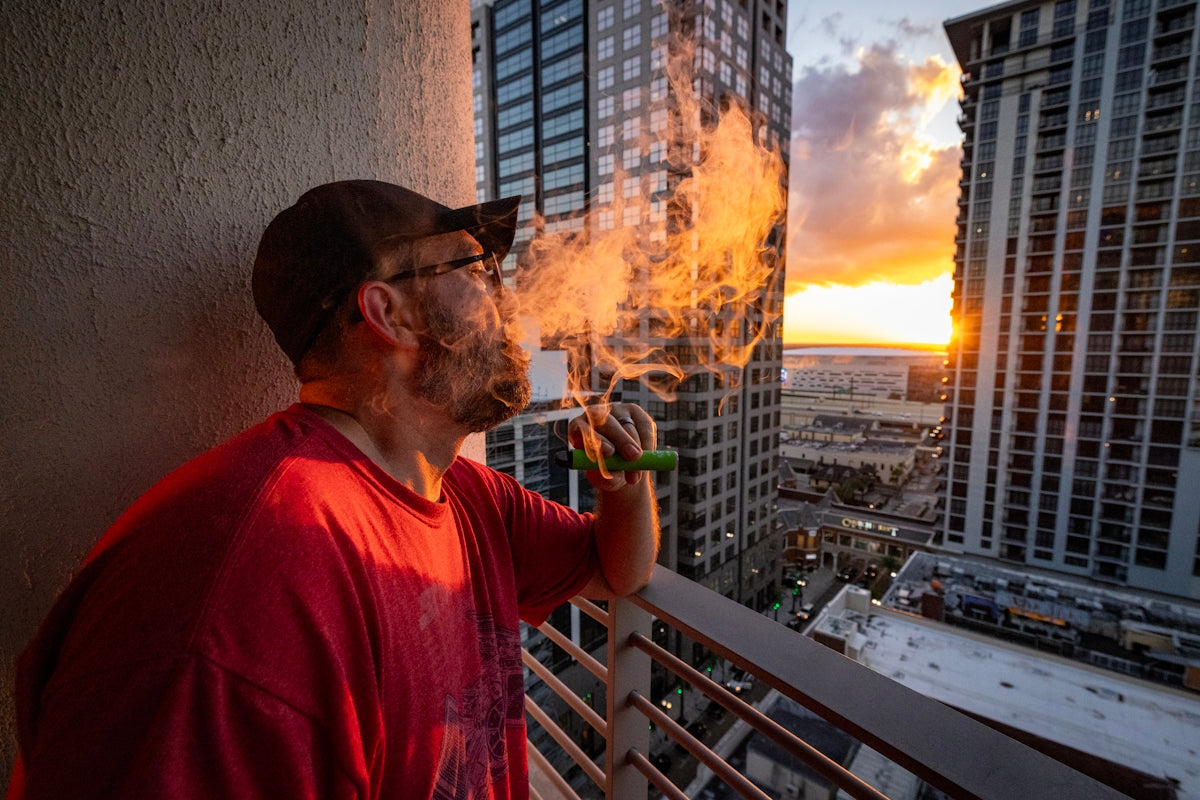Man vaping on balcony with city skyline sunset